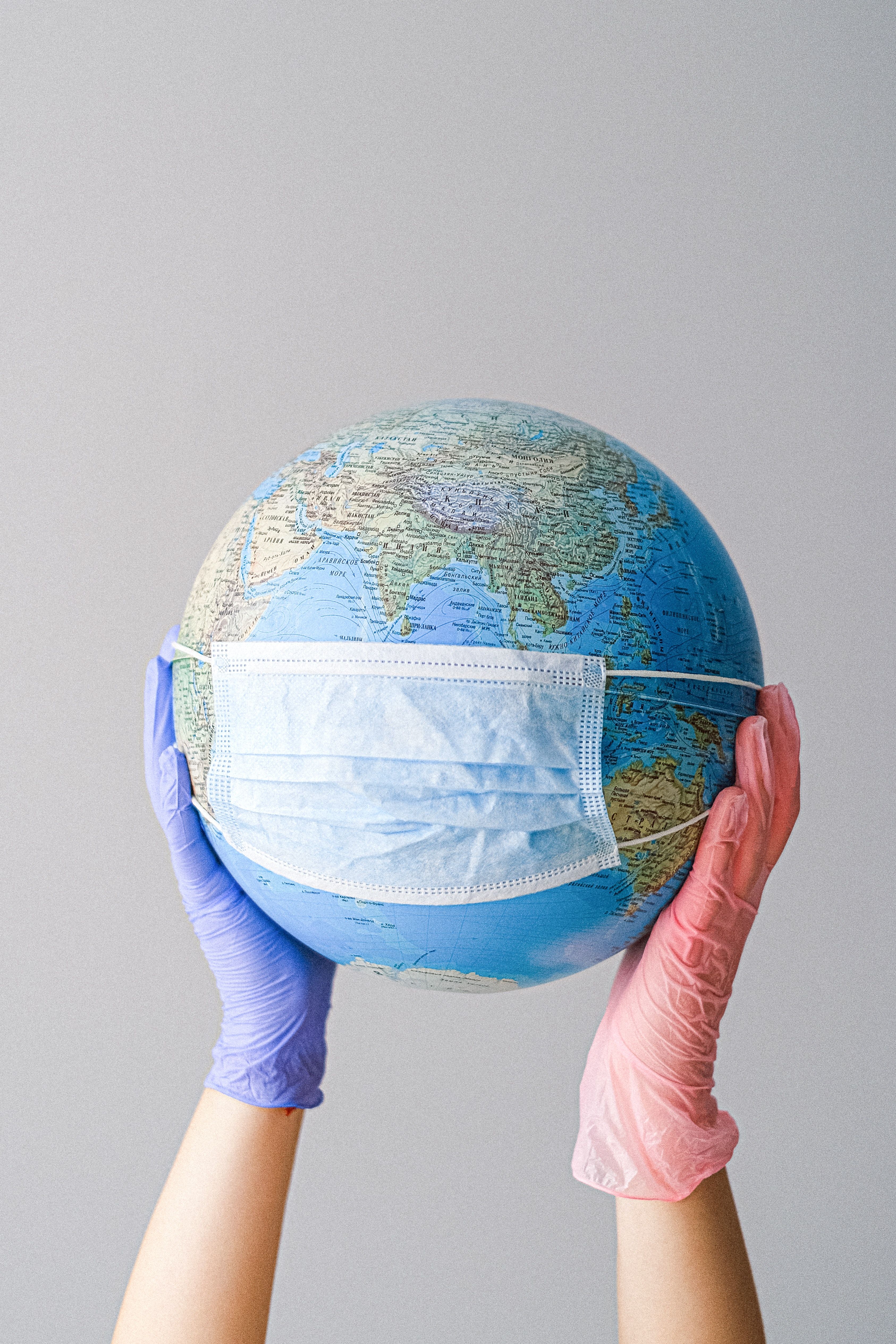 Hands With Latex Gloves Holding a Globe with a Face Mask · Free