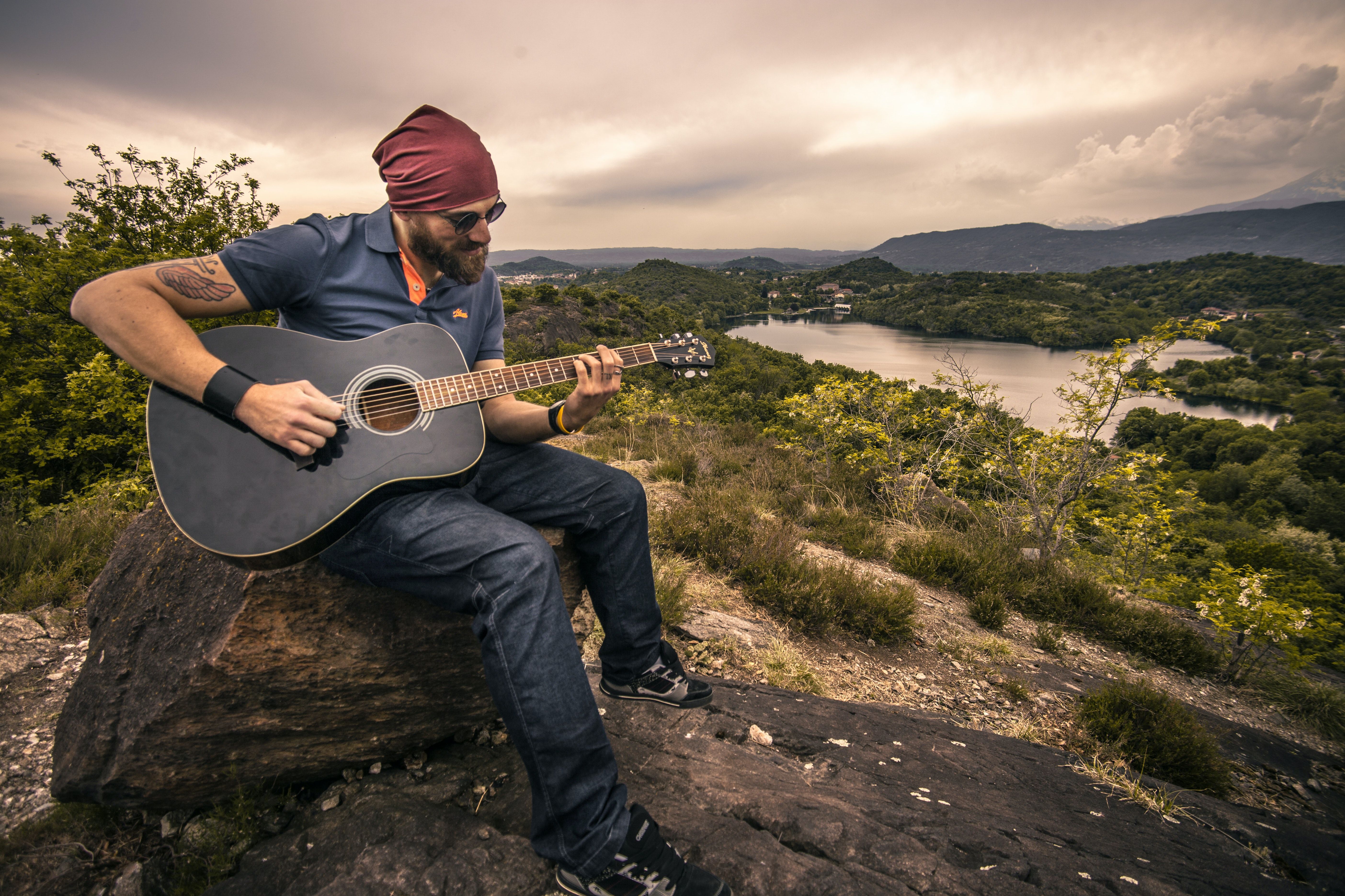 Man Playing Guitar Sitting on Brown Rock · Free