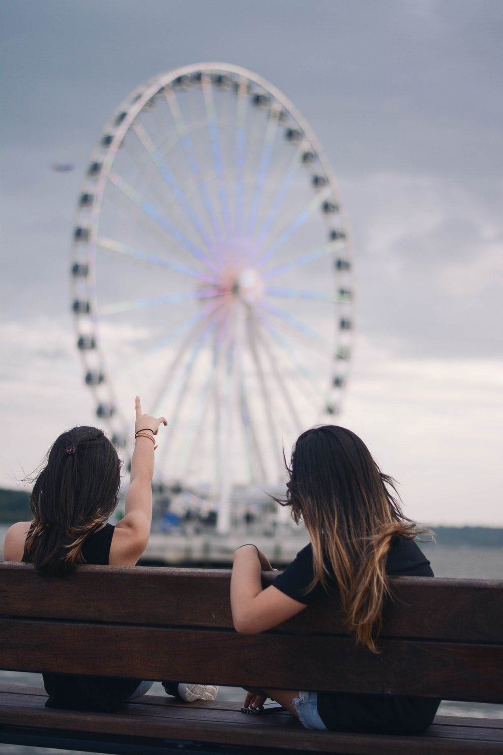 two women sitting on bench pointing white and blue Ferris wheel photo