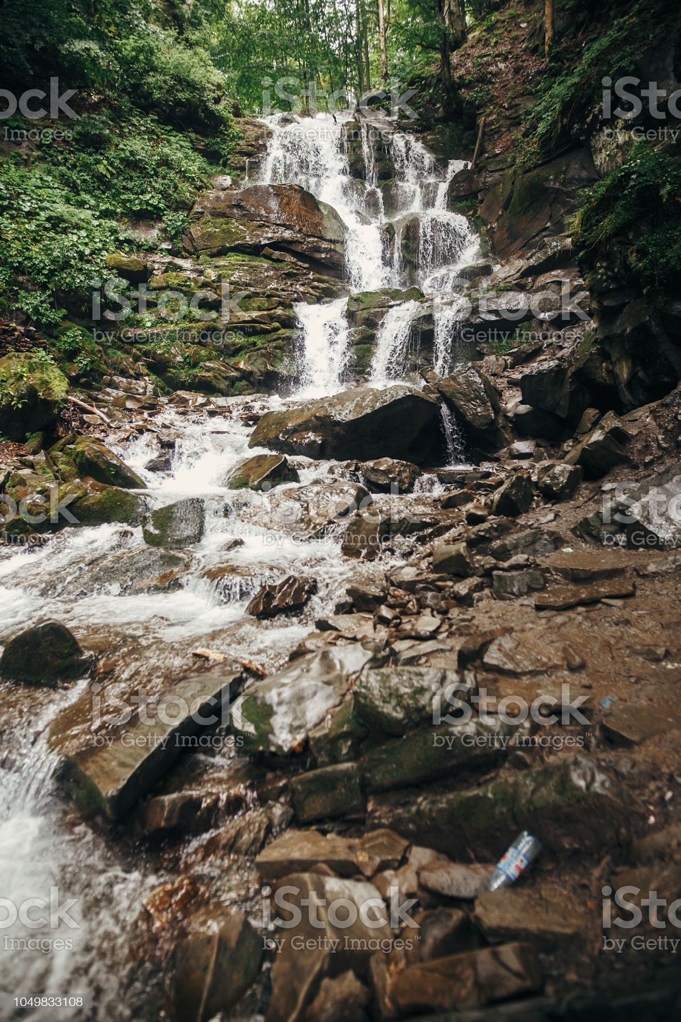 beautiful waterfall on river in forest in mountains. cascades river with water motion and rocks. beautiful scenery landscape of river in woods under summer sun light. vertical rainforest wallpaper