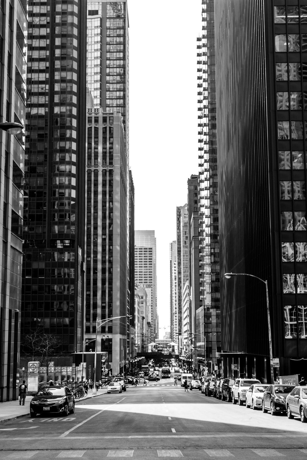 grayscale photo of road in between of tall buildings with vehicles photo