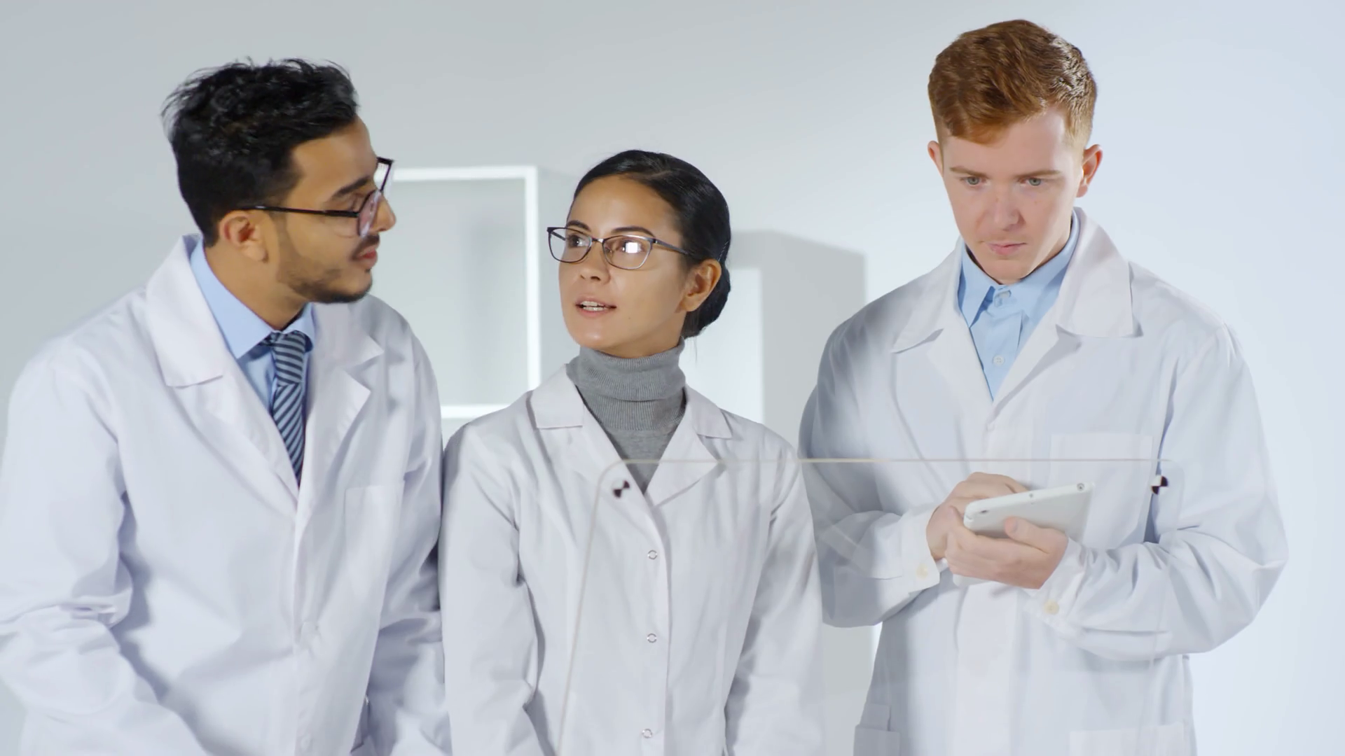 Medium shot of three diverse scientists in lab coats standing together at invisible AR display of futuristic computer and talking. Video suitable for adding AR graphics Stock Video Footage