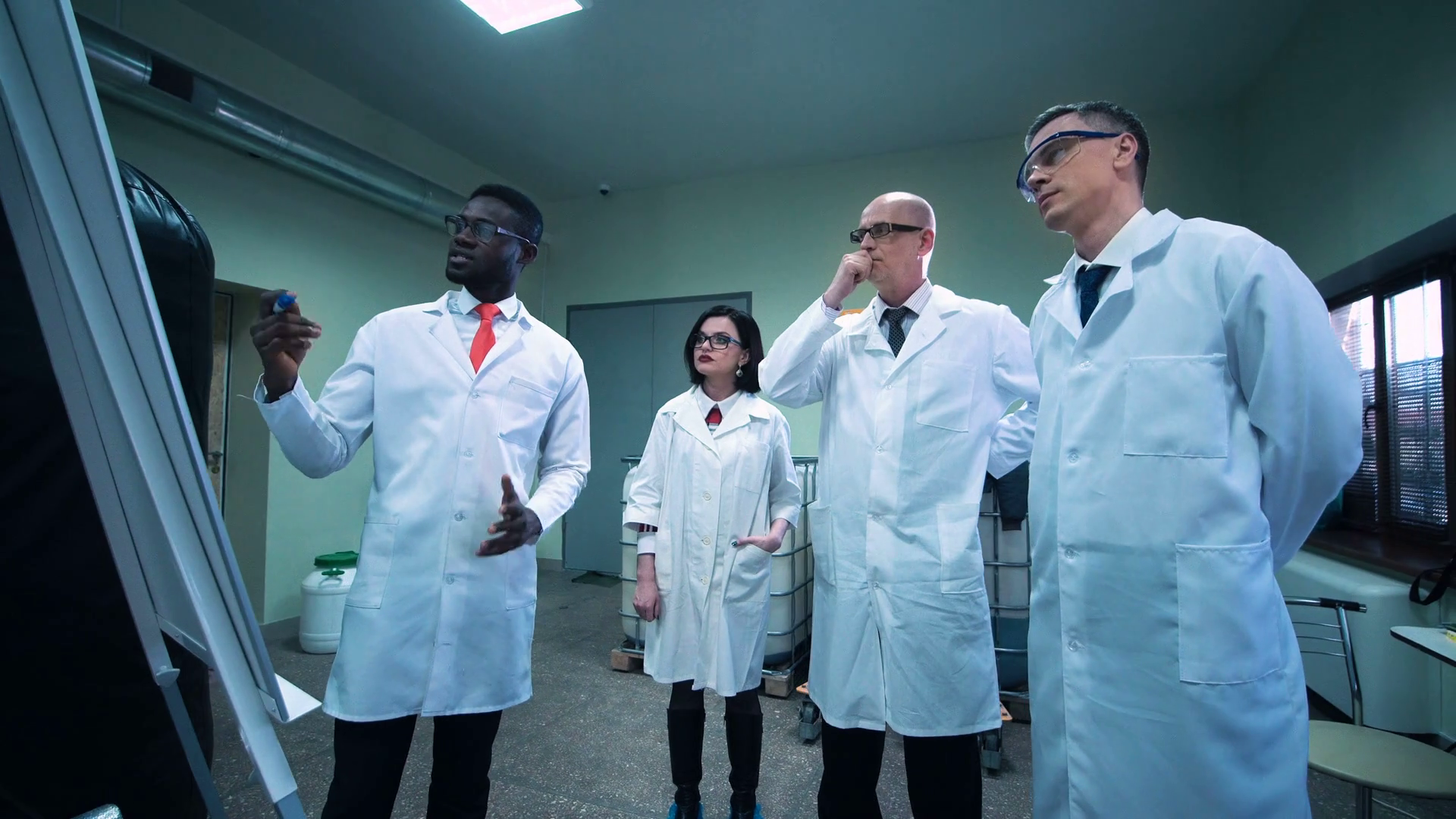 Four scientists in white lab coats standing indoors and discussing project that black man showing on white board Stock Video Footage
