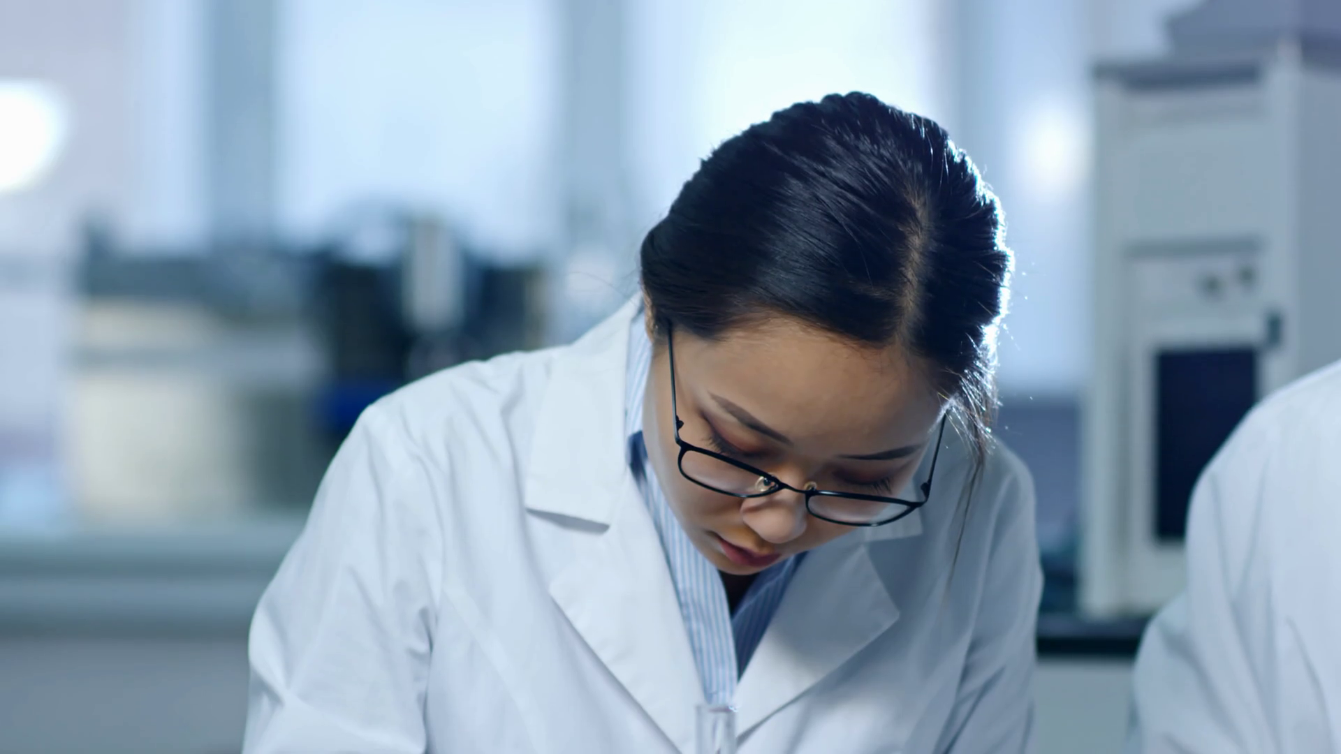 Tilt down shot of young Asian woman in lab coat and glasses writing down research details when working in laboratory Stock Video Footage