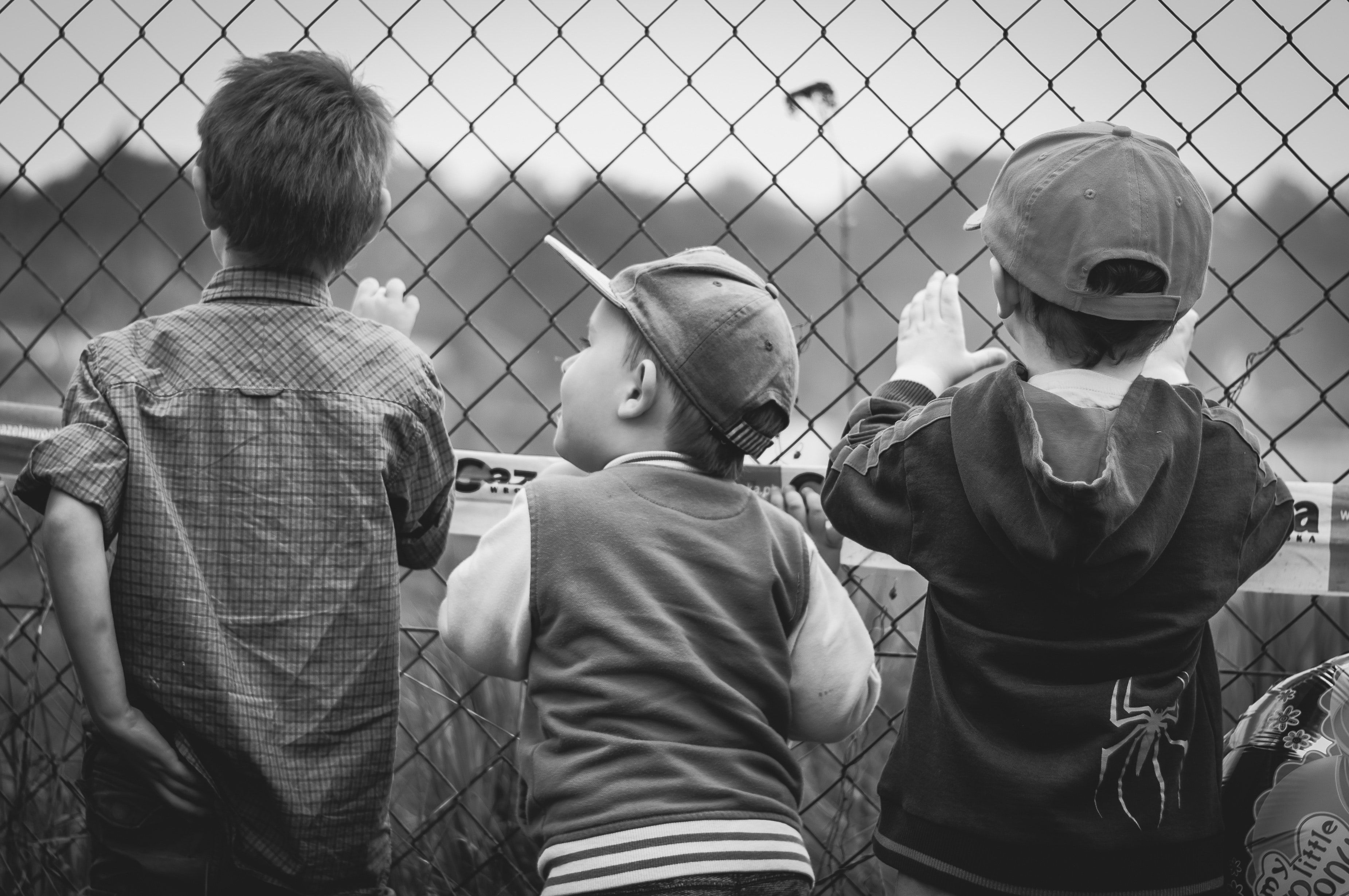 Grayscale Photography of Three Boys Facing Towards Fence · Free