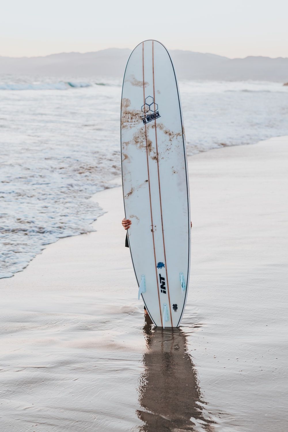 white surfboard upright on seashore during daytime photo