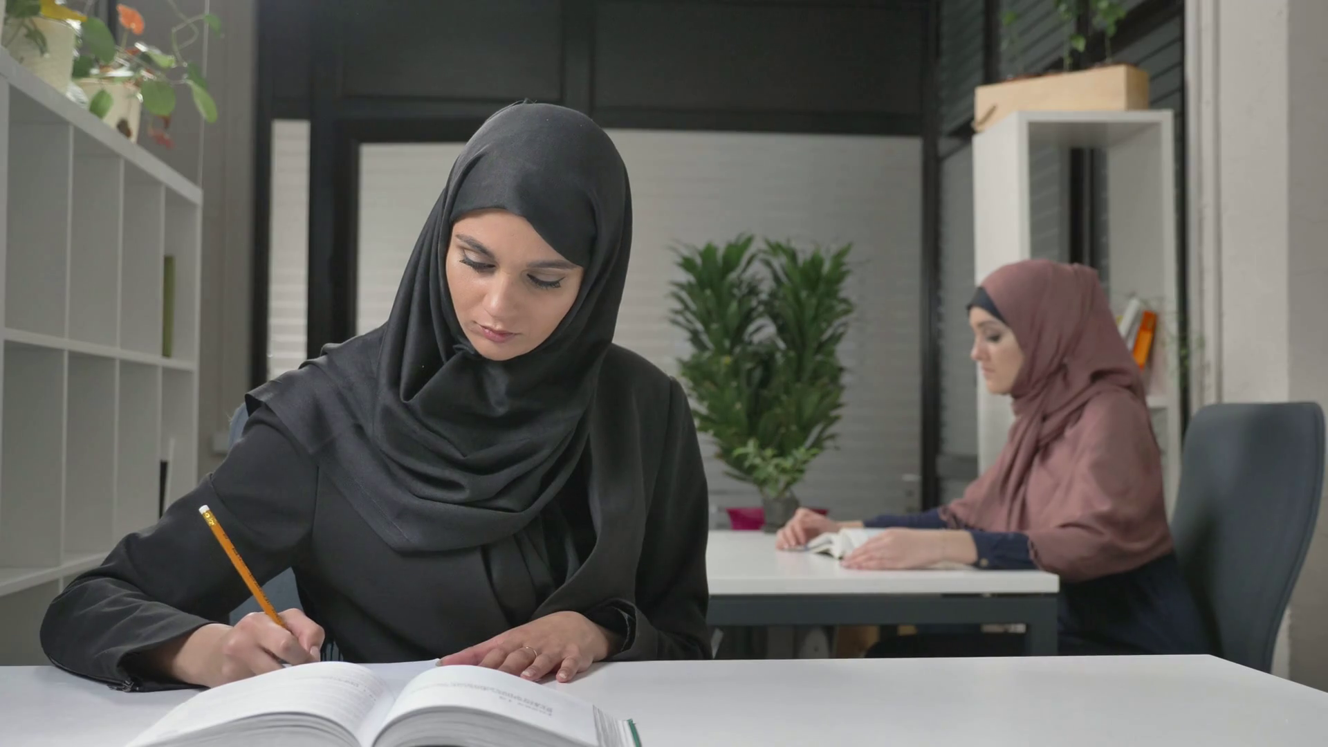 A young beautiful girl in a point and a black hijab will write off in Arabic. Arab women in the office 60 fps Stock Video Footage
