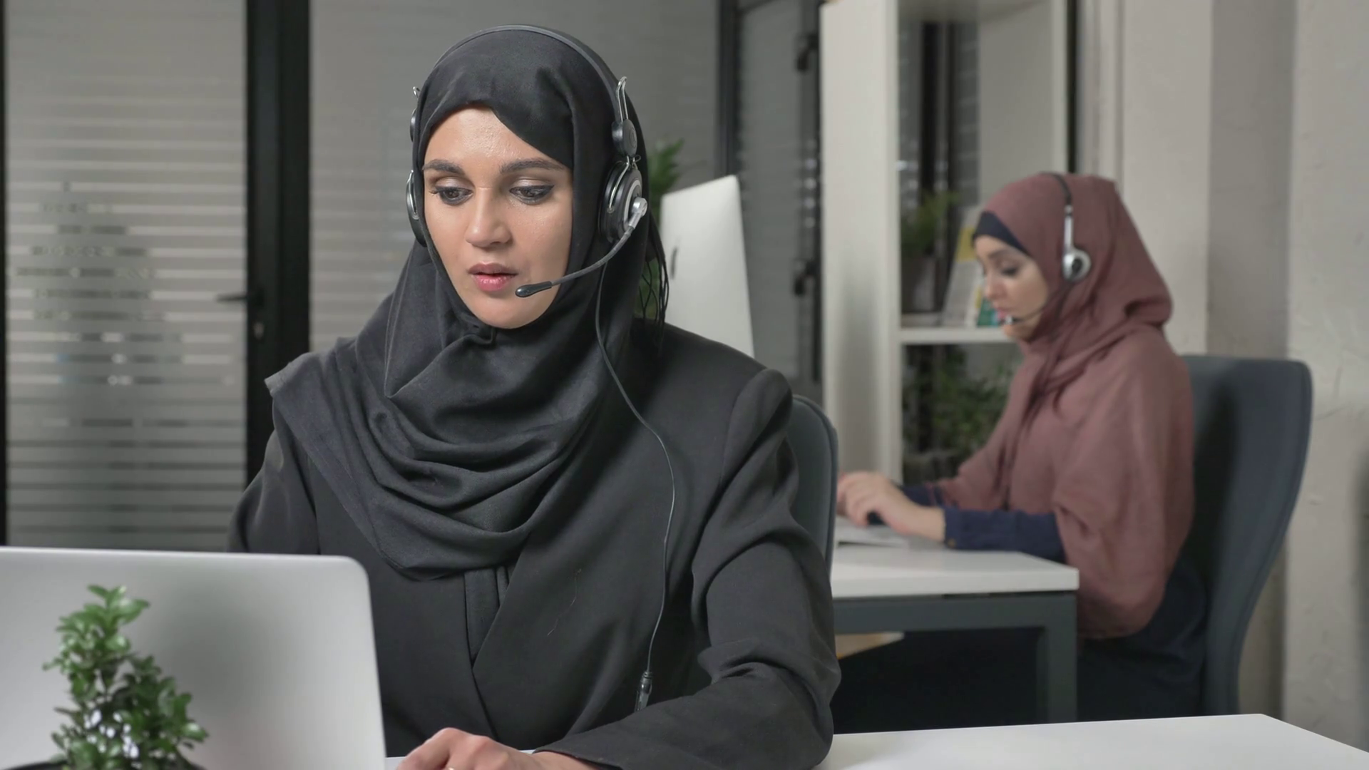 Young beautiful girl in black hijab with headset answers a call center. Arab women in the office. Concept 60 fps Stock Video Footage