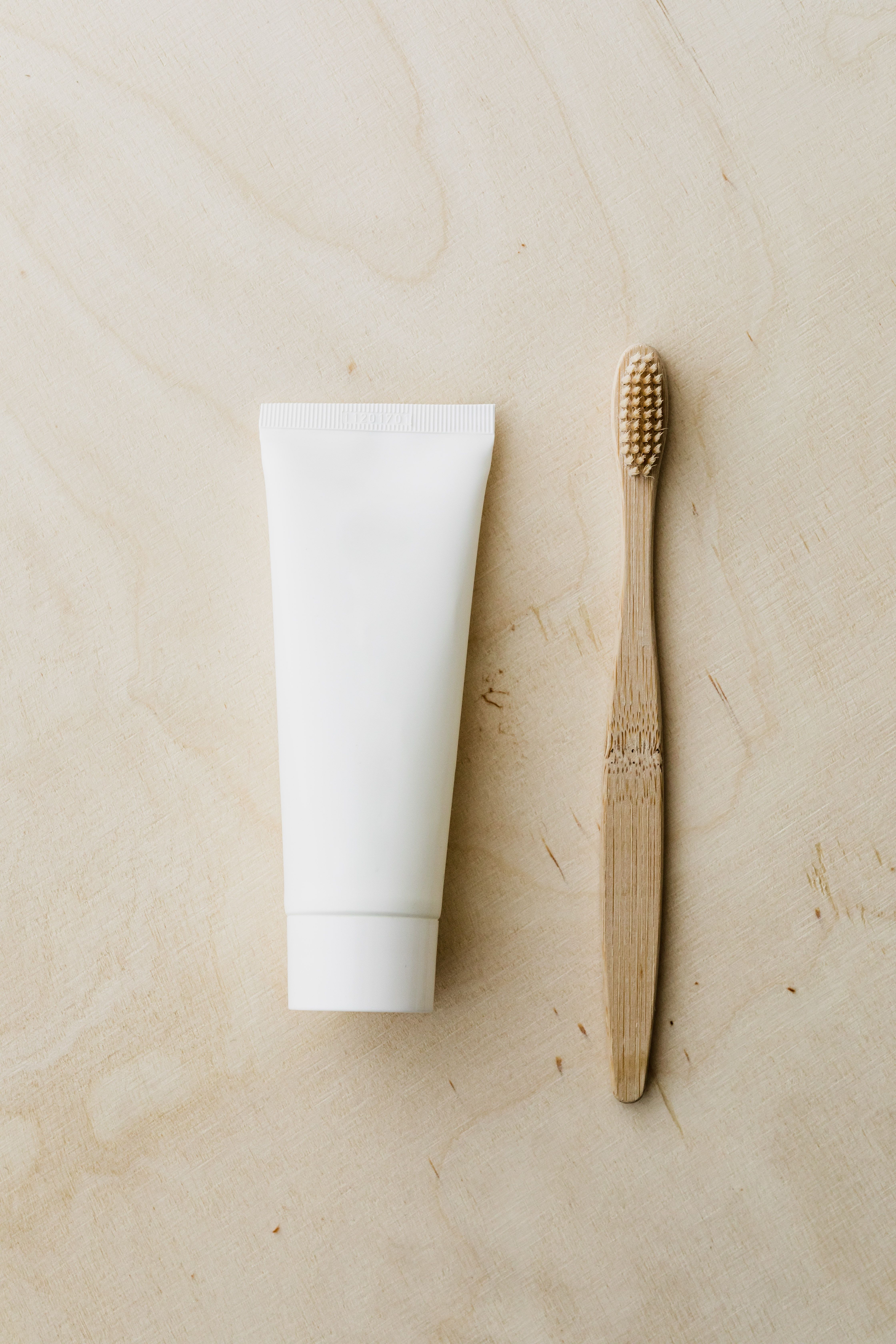 White toothpaste tube and bamboo toothbrush on wooden surface · Free