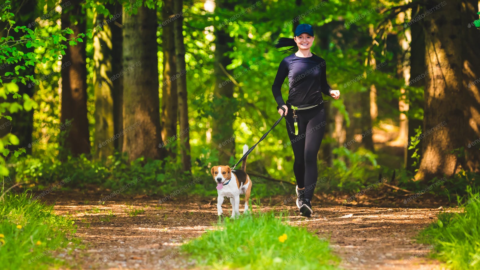Sport girl is running with a dog (Beagle) at the spring sunny day on the forest path. photo by IciakPhotos on Envato Elements