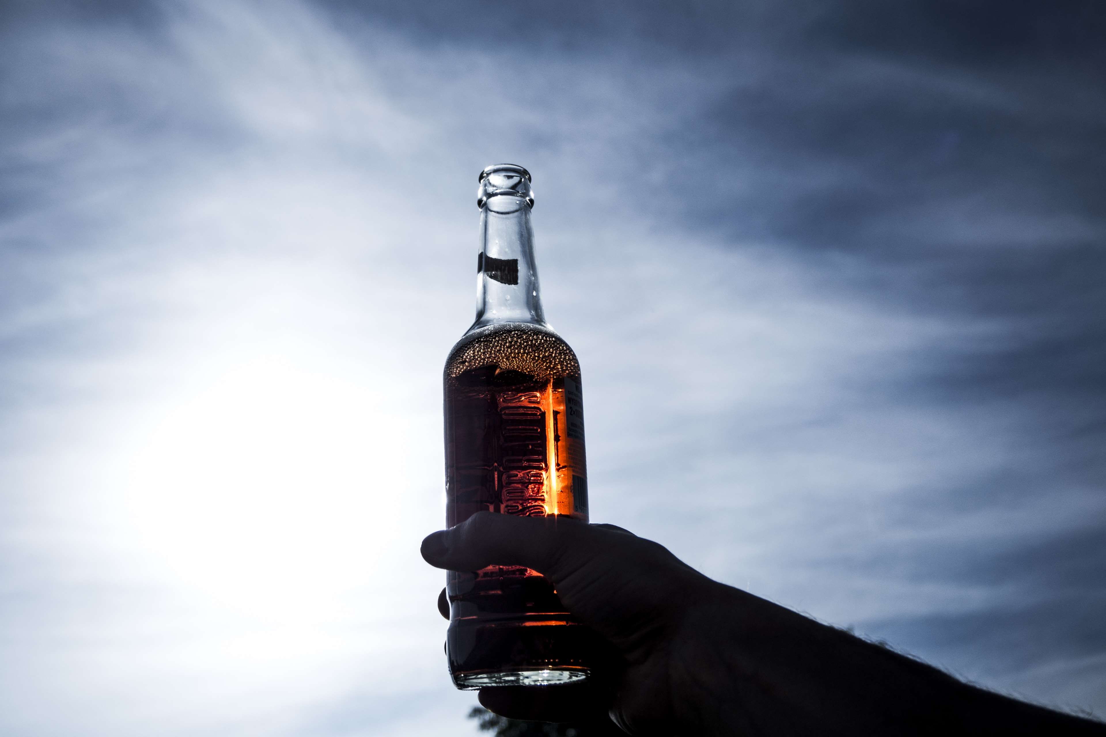 alcohol, beer, beverage, bottle, clouds, dark, daylight, glass, hand, light, liquor, outdoors, sky 4k wallpaper