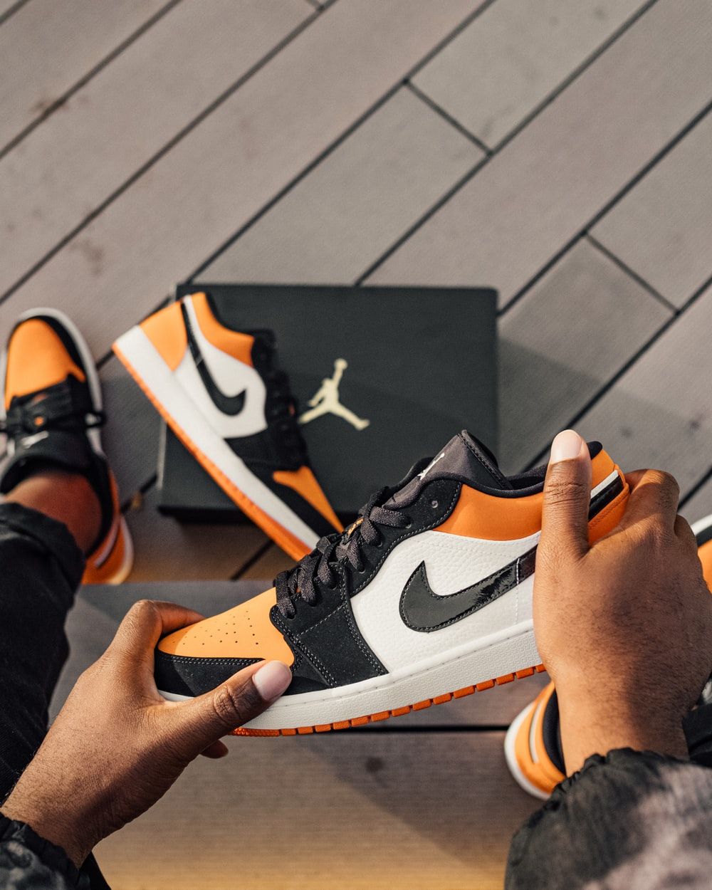Person Sitting And Holding White, Orange, And Black Air Jordan 1 Low Top Sneaker Photo