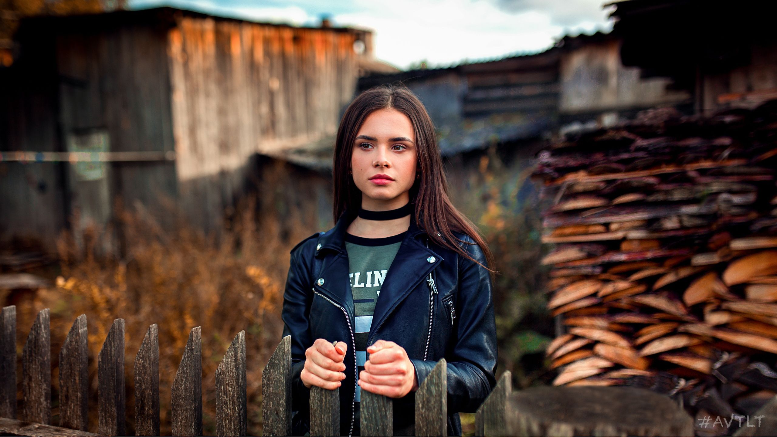 Wallpaper, women, model, brunette, portrait, outdoors, leather jackets, black jackets, depth of field, looking away, necklace, T shirt, wood, fence, brown eyes, Aleksandr Suhar 2560x1440