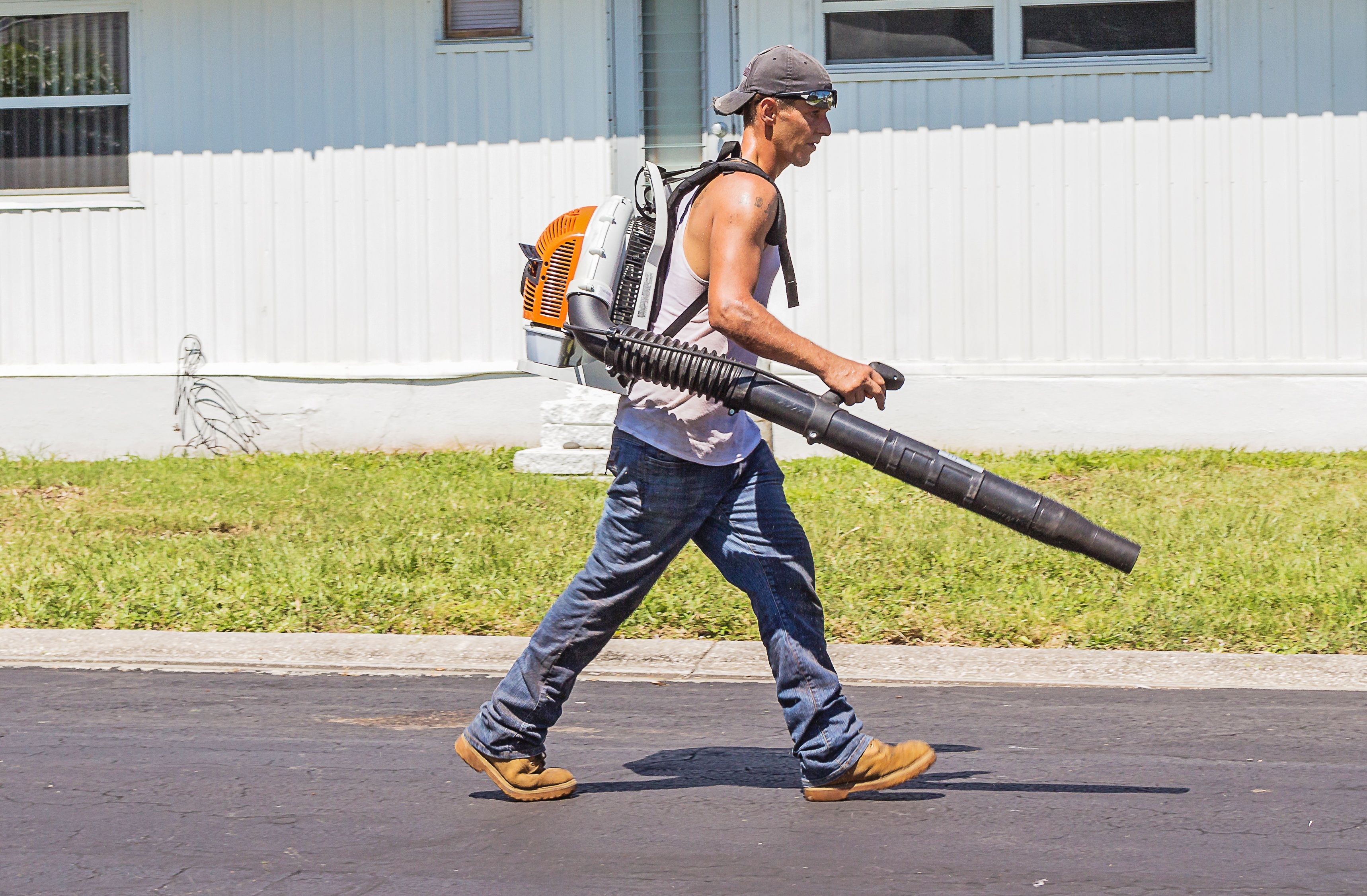 Man in White Tank Top and Blue Denim Pants With Leaf Blower Outdoors during Daytime · Free