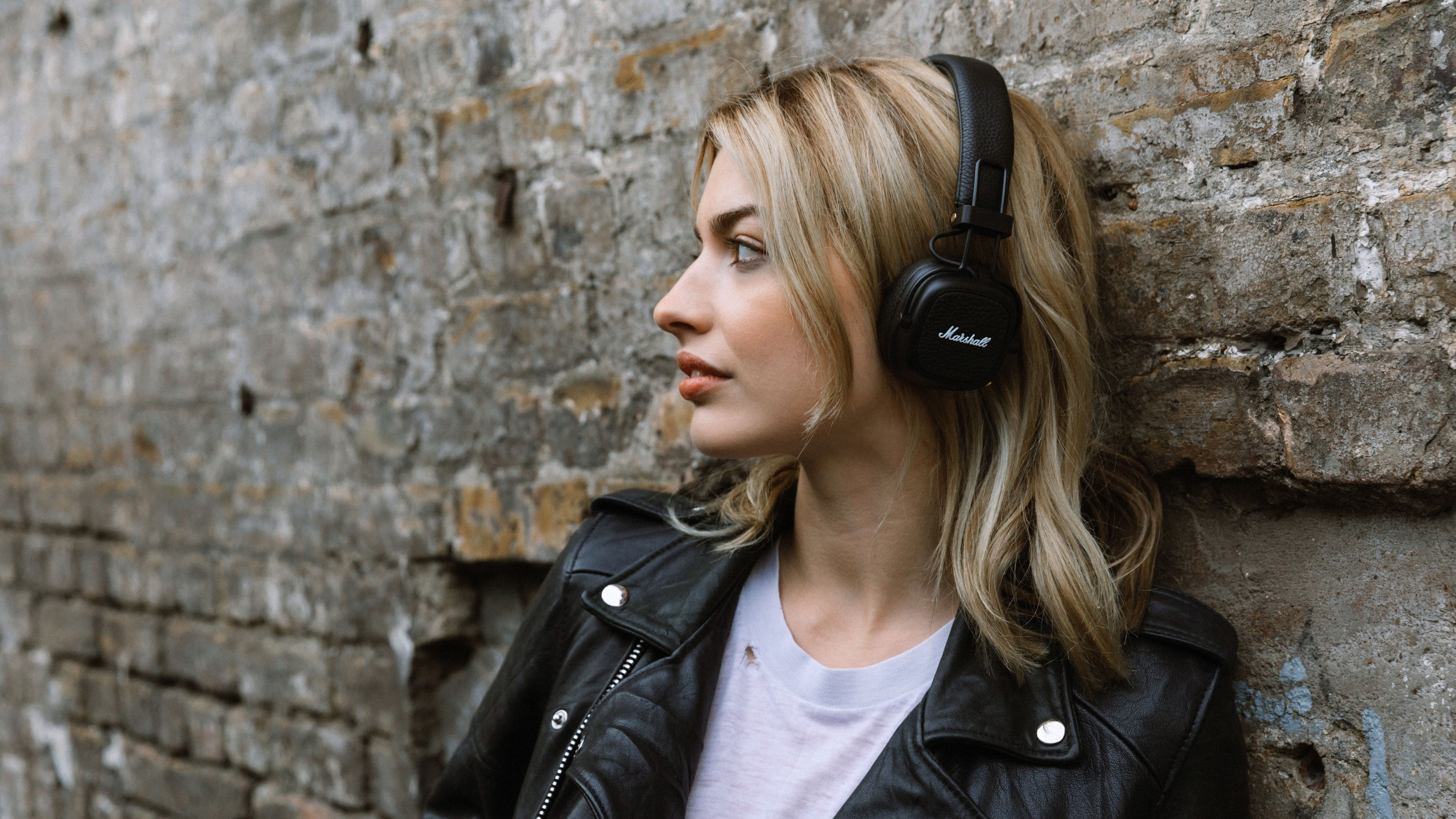Black Leather Jacket Wearing Blonde Hair Girl With Headphone Is Leaning On A Dirtly Wall 4K HD Model Wallpaper