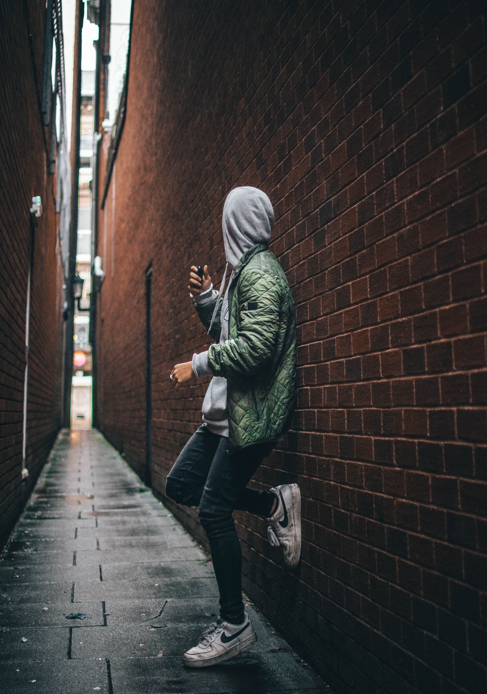 man wearing green hooded jacket standing beside the wall photo