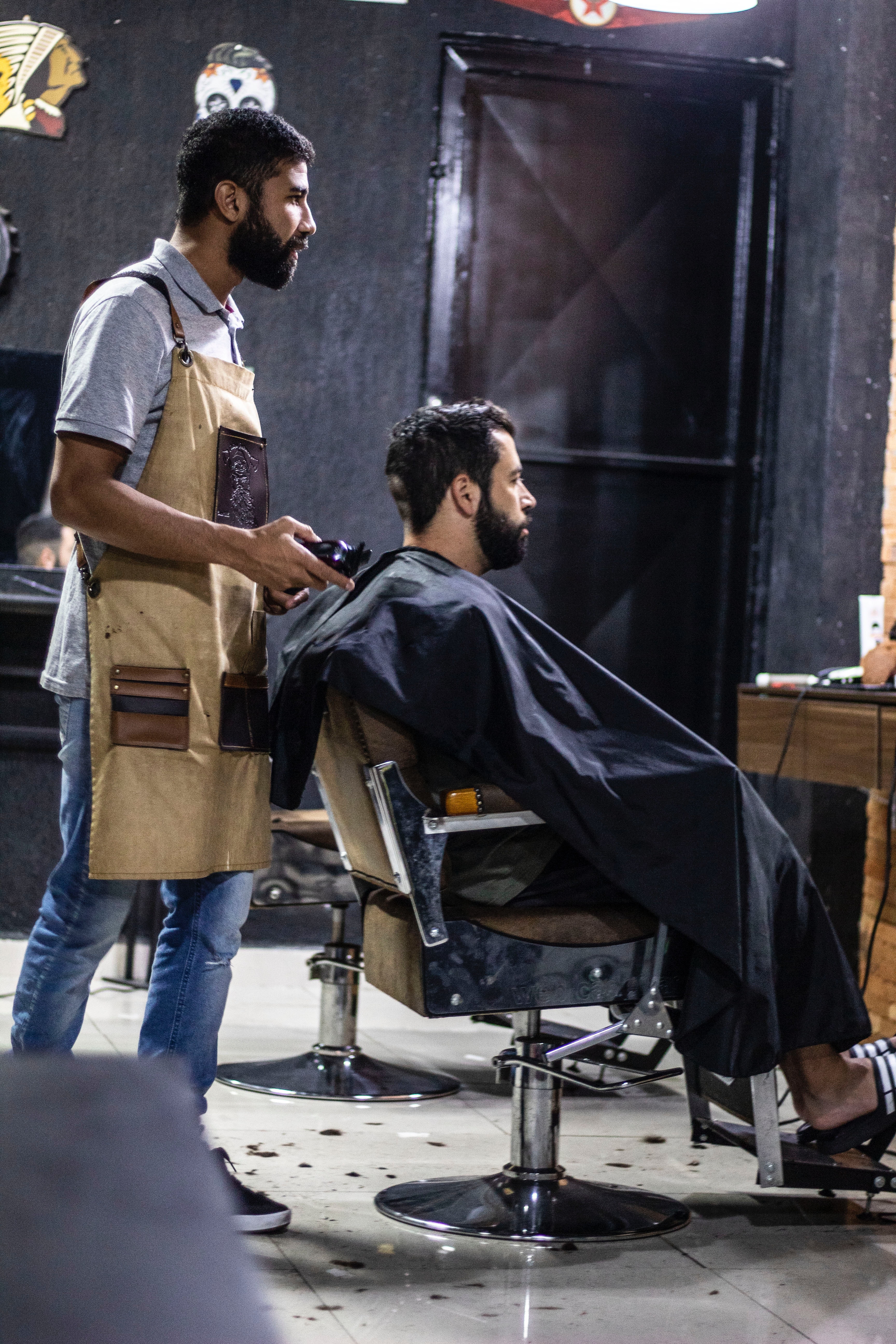 Man Wearing Brown Apron and Man Sitting on Gray Stainless Steel Barber's Chair · Free