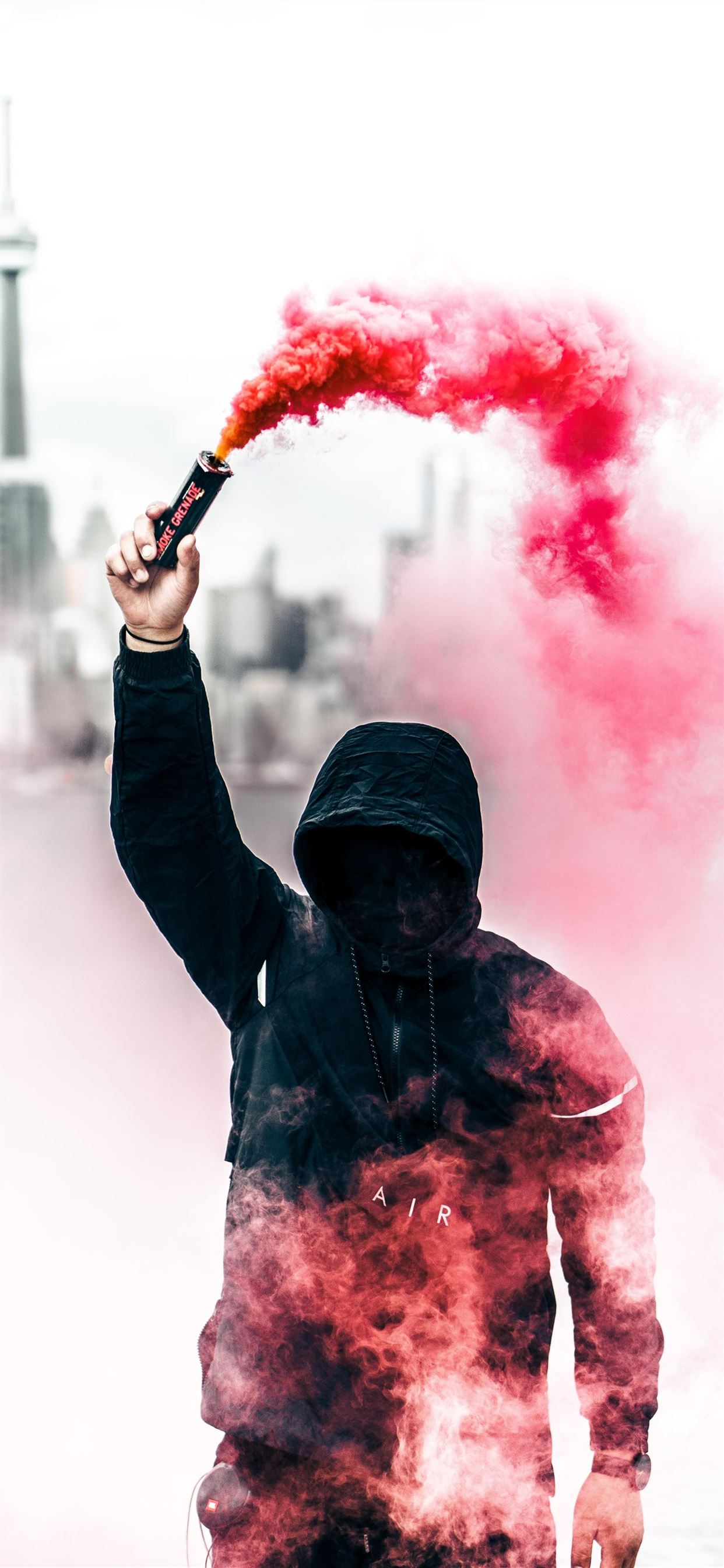 person wearing black and red hoodie holding smoke. iPhone 11 Wallpaper Free Download