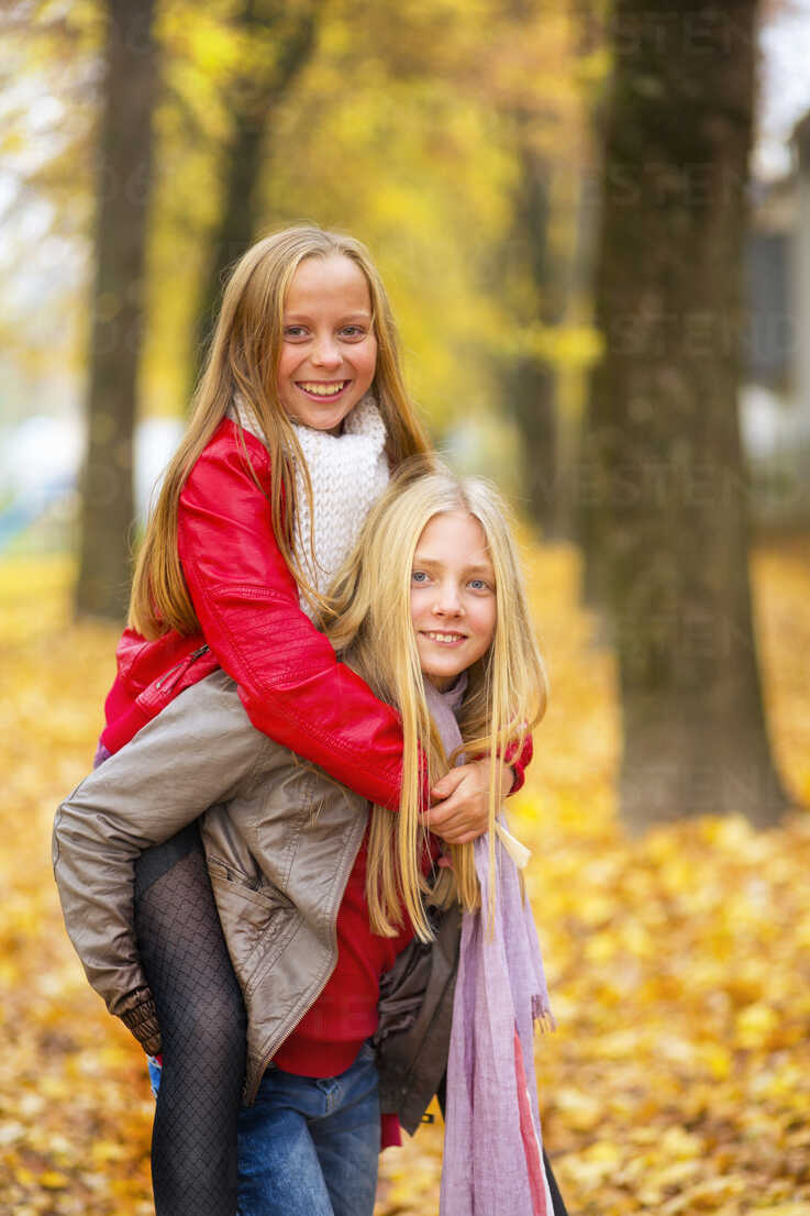 Girl giving her best friend a piggyback ride in autumn