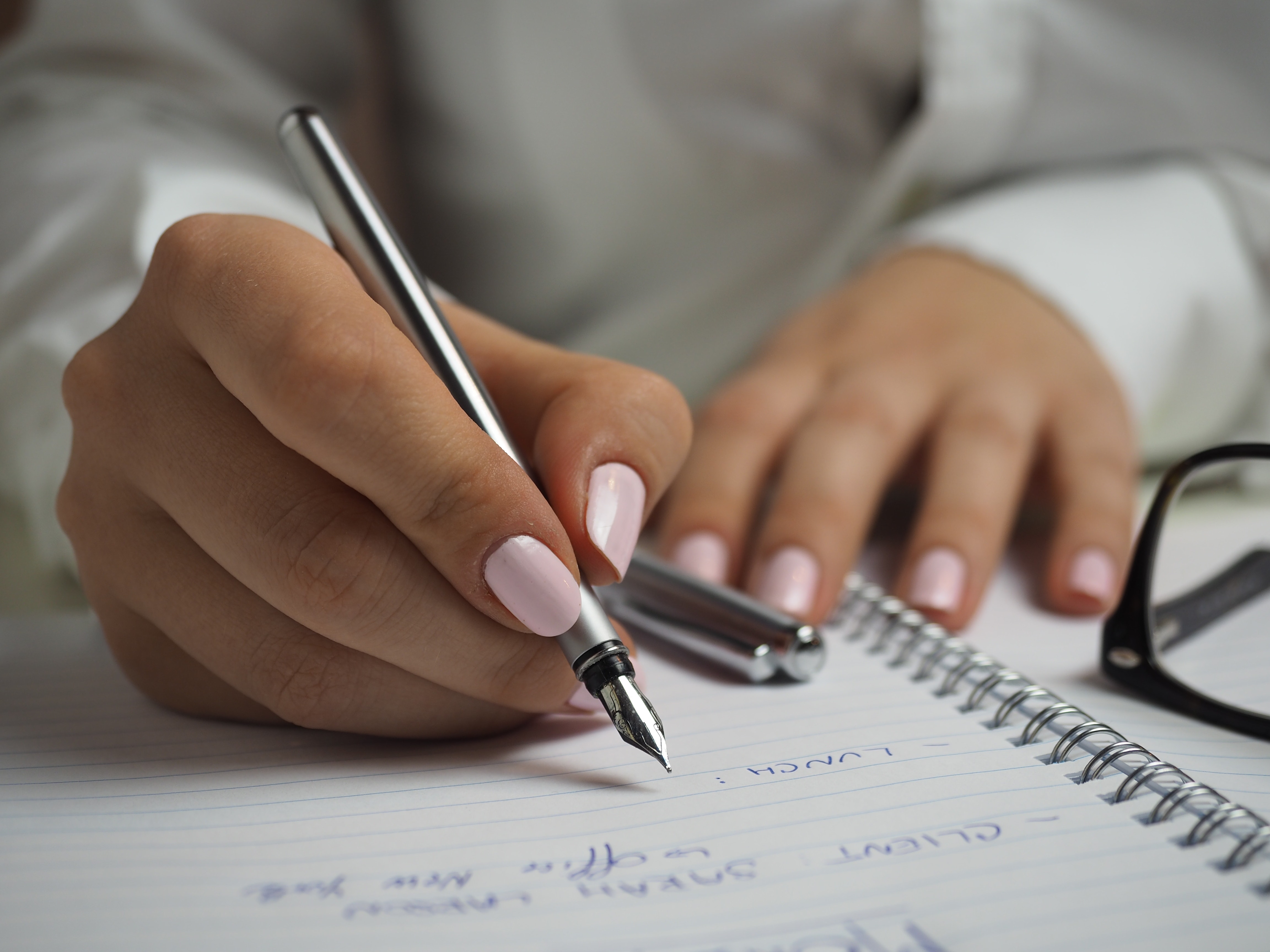 Woman in White Long Sleeved Shirt Holding a Pen Writing on a Paper · Free