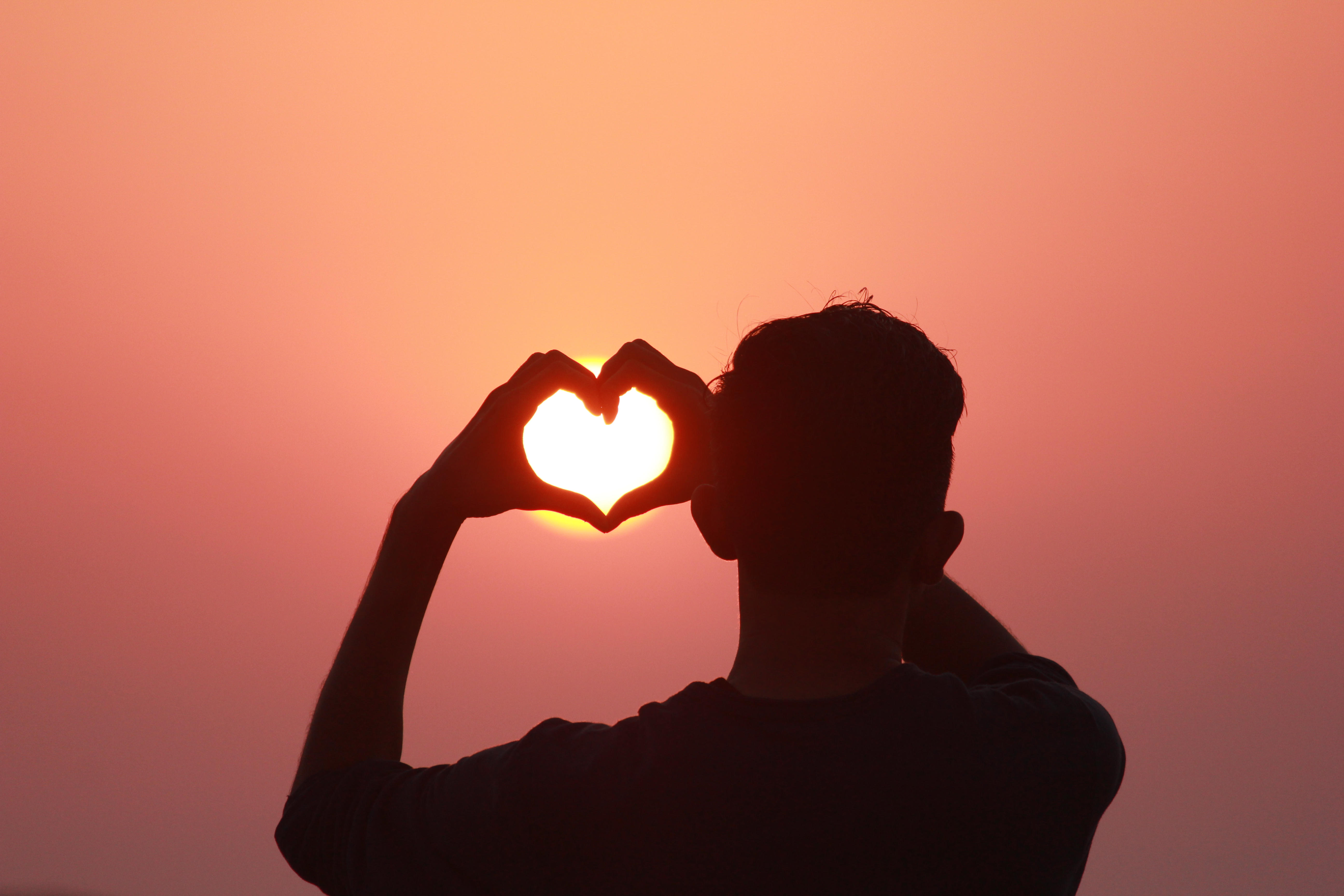 Man making heart gesture with hands in sunset · Free